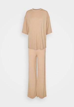 Beżowy, oversize'owy T-shirt z krótkim rękawem w zestawie z pasującymi spodniami o szerokich nogawkach, prezentowany na jednolitym białym tle.