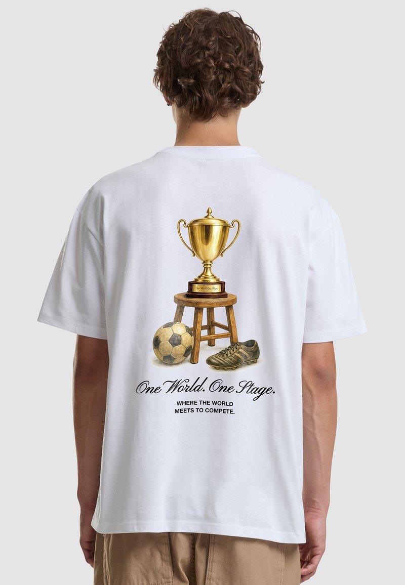 Personne portant un t-shirt blanc avec un design de trophée en or dans le dos, assise sur un tabouret en bois, ballon de football vintage, crampon, et texte sur une compétition mondiale.