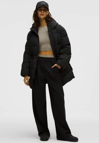 Giacca a vento nera con design trapuntato, abbinata a un top grigio corto e pantaloni neri larghi. Gli accessori includono un cappellino nero.