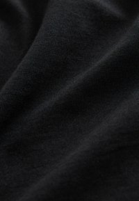 Primer plano de una suave tela de punto negra con una textura fina visible y sutiles pliegues que crean sombras suaves.