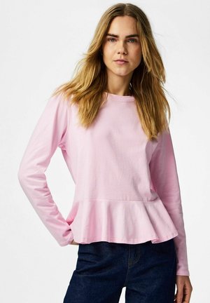 Chemise rose clair à manches longues avec un col rond et un ourlet peplum, en tissu lisse. Associée à un jean en denim foncé.
