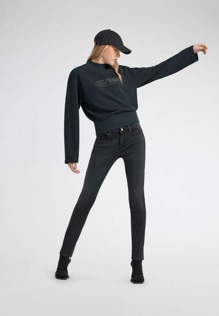 Felpa nera con vestibilità rilassata e dettaglio del logo, abbinata a jeans neri aderenti e un berretto nero. Tessuto liscio e design minimale.