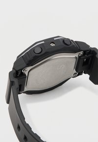 Czarny sportowy zegarek z gumowym paskiem, metalowym tyłem koperty, dwoma przyciskami i fakturowaną powierzchnią. Charakteryzuje się solidnym, wytrzymałym designem.