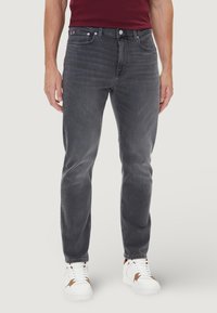 Jeans in denim grigio con vestibilità a gamba dritta, caratterizzati da un classico design con cinque tasche e sfumature sottili. Abbinati a sneakers bianche.