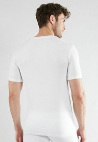 Witte getailleerde T-shirt van gladde katoen, met korte mouwen en een ronde hals. De achterkant is naadloos met minimale stiksels.