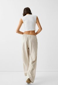 Bílý zkrácený top s krátkými rukávy, který je kombinován s volnými, světle béžovými kalhotami s elastickým pasem. Hladká textura po celém povrchu.