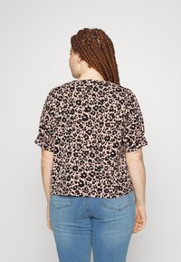 Camisola de manga curta em tecido rosa com padrão de leopardo preto; apresenta um corte descontraído e mangas enroladas, combinada com jeans azuis.