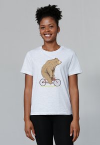 Hellgraues T-Shirt mit einer Bärenillustration auf einem roten Fahrrad. Kurze Ärmel, Rundhalsausschnitt, weicher Stoff. Schwarze Hosen darunter getragen.
