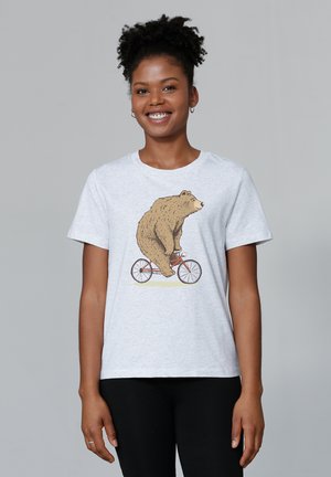 T-shirt gris clair avec une illustration d'un ours sur un bicycle rouge. Manches courtes, col rond, tissu doux. Pantalons noirs portés en dessous.