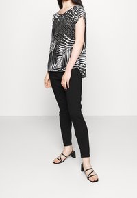 Top a maniche corte con stampa in bianco e nero e design fluido, abbinato a pantaloni slim-fit neri e sandali con tacco neri a strappo.
