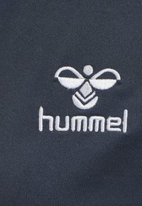 Mörkblått tyg med en vit broderad logotyp av en bi-design ovanför ordet "hummel" i små bokstäver.