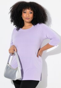 Tunic in lavanda, tessuto leggero con maniche a tre quarti, tasche laterali, abbinata a una borsa argentata. Texture liscia e vestibilità comoda.