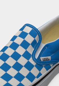Slip-on παπούτσι Vans με μπλε και λευκό καρό σχέδιο, λευκή σόλα και εμφανές ταμπελάκι με το λογότυπο Vans στο πλάι.