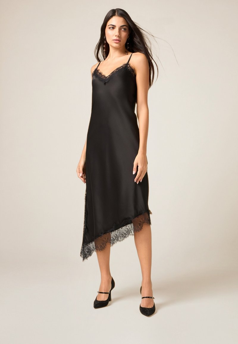Svart satinklänning med spetskant längs den asymmetriska fållen. Har tunna band och en v-ringning för en elegant och flödande silhuett.