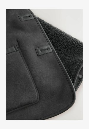 Zwarte neplederen deken met een gestructureerd oppervlak, voorzien van een zachte, donkere fleece binnenkant en twee lussen voor bevestiging. Randen zijn afgewerkt met leer.