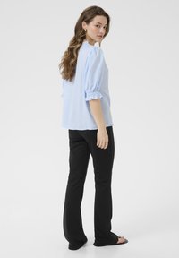 Blusa azul clara con mangas abullonadas, puños con volantes y un corte relajado, combinada con pantalones negros de pierna recta. Diseño simple y limpio.