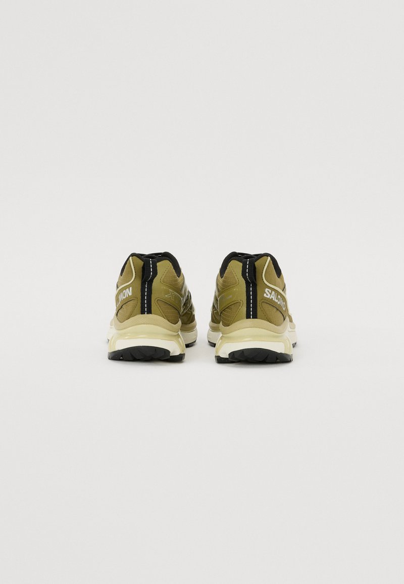 Olivgrüne Sportschuhe mit schwarzen Akzenten und weißem Logo, strukturiertes Obermaterial und gepolsterte Sohle; verfügen über ein langlebiges Profil für Traktion.