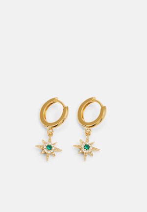 Boucles d’oreilles créoles en or avec pendentifs en forme d’étoile comprenant une pierre centrale verte et de petites pierres transparentes sur un fond gris clair.