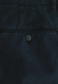 Tessuto dei pantaloni blu scuro con una tasca sul retro dotata di un bottone rotondo a quattro fori. La texture è liscia con una leggera lucentezza.