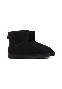 Botines de ante negro con un perfil bajo, punta redonda y suela de goma. Presentan un tirador en la parte posterior y un sutil detalle de costura.