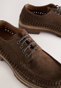 Chaussures en daim marron avec un design tissé sur les côtés, lacets ronds et semelle en caoutchouc robuste. Fini texturé pour plus de détails.