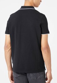 Black polo shirt with a collared neck, short sleeves, and white trim along the collar and sleeve edges. Smooth cotton fabric, casual fit.