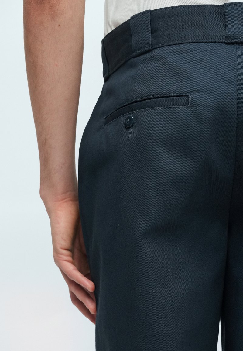 Marineblaue Hose mit glatter Textur, ausgestattet mit einer Rückenpocket mit Knopfverschluss und einem flachen Bündchen.