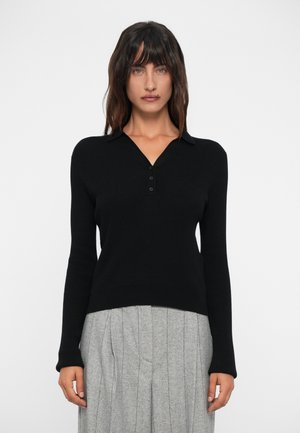 Pulover negru din tricot cu model canalat, cu guler în V și placket cu trei nasturi. Mâneci lungi și tiv ajustat. Purtați cu o fustă plisată gri.