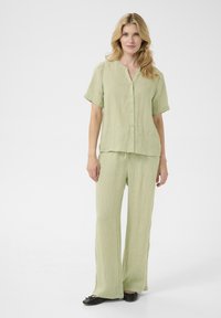 Set in lino di colore verde chiaro composto da due pezzi, con una camicia a maniche corte con bottoni e pantaloni a gamba larga, dal fit rilassato e una texture sottile.