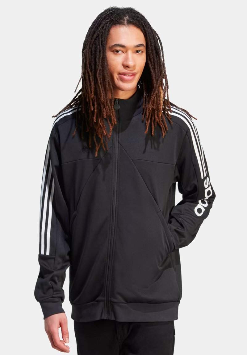 Chaqueta negra con cremallera hecha de tela suave, con acentos en blanco de tres rayas en las mangas y un logo bordado en el pecho.
