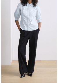 Light blue, puff-sleeve blouse with a button-up front and collar, paired with black wide-leg trousers and pointed black shoes.
