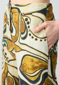 Pantalons en mélange de lin avec un grand motif abstrait en jaune, brun et bleu. Comprend des poches latérales et une fermeture éclair à la taille.