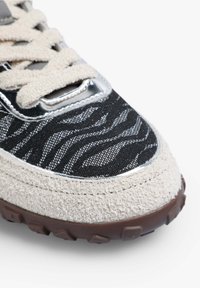 Buty sportowe z szarym zamszowym spodem, czarną tekstylną cholewką w wzór zebry, metalowymi akcentami i brązową gumową podeszwą zapewniającą przyczepność.