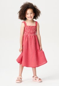 Rot-weiße gestreifte Kleid mit gerafftem Oberteil, breiten Trägern und einem schwingenden, knielangen Rock; kombiniert mit rosa Sandalen.