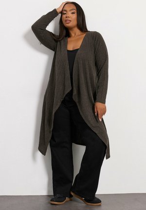 Cárdigan largo abierto en tejido texturizado de color verde oliva oscuro, combinado con una blusa negra y pantalones anchos negros. Presenta un diseño fluido.
