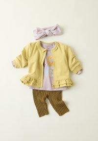 Chaqueta amarilla con cremallera y bajo con volantes, camisa lila con gráfico de "LOVE", pantalones marrones acanalados y una cinta para la cabeza texturizada en lila.