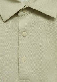 Ljusgrön polo skjorta med en texturerad tyg, klassisk krage, tre beiga knappar och prydlig sömnad längs placket.