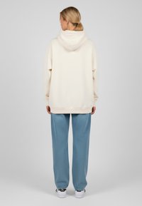 Felpa crema con un ampio cappuccio, polsini a costine e una vestibilità rilassata, abbinata a pantaloni della tuta in denim azzurro chiaro e scarpe da ginnastica bianche.
