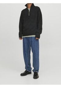 Czarny, dziergany sweter na zamek z prążkowanymi mankietami, zestawiony z luźnymi, jasnoniebieskimi dżinsami oraz czarnymi butami sznurowanymi.