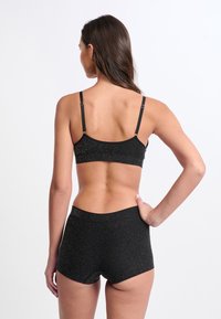 Czarny biustonosz braletka z metalicznymi drobinkami, z regulowanymi ramiączkami, w połączeniu z dopasowanymi czarnymi szortami, wszystko wykonane z miękkiego, elastycznego materiału.