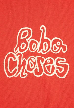 Fondo de tela roja con texto ondulado de contorno blanco que dice "Bobo Choses" en una fuente juguetona e irregular.