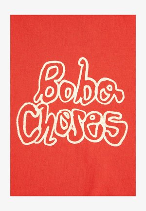 Red fabric background with white outlined wavy text reading "Bobo Choses" in a playful, irregular font.