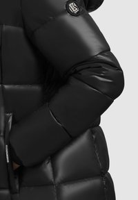 Black puffer jacket featuring a shiny, quilted texture with a round logo badge on the sleeve and side pockets for added functionality.