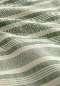 Baumwollstoff mit abwechselnd hellgrünen und weißen Streifen, der eine strukturierte Oberfläche und ein weiches, leicht zerknittertes Aussehen aufweist.