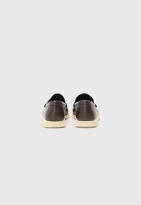 Paire de chaussures en cuir noir à enfiler avec semelles couleur crème, vues de dos sur un fond gris clair uni.