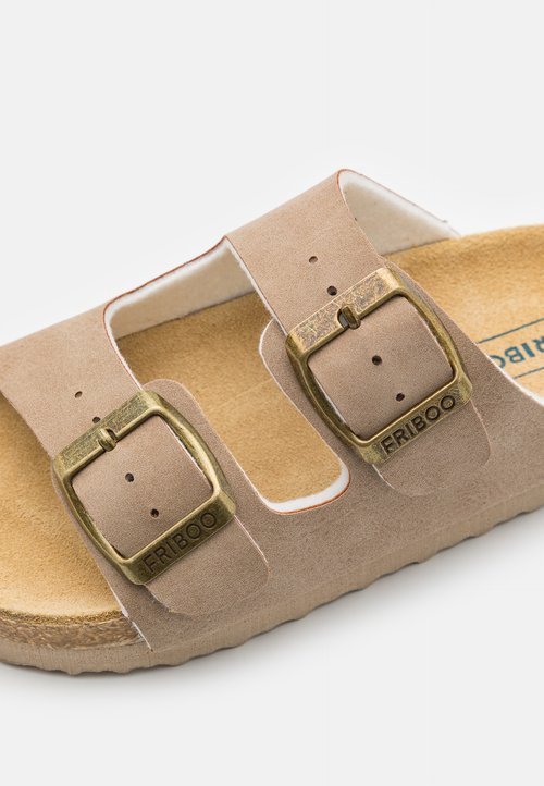 Sandale beige clair avec des fermetures à boucle brune réglables, semelle en liège et design découpé. Tige en suède doux avec une finition texturée.
