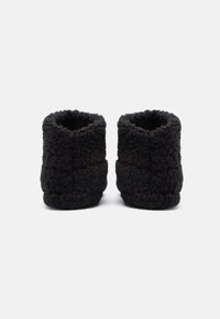 Črne, puhaste copate za gležnje s teksturirano zunanjostjo, zaobljenimi odprtinami in izrazitimi šivi, zasnovane za udobje in toploto.