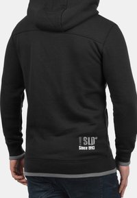Felpa nera con cappuccio, dal design aderente, polsini a costine, orlo grigio e dettaglio bianco del logo sul retro. Realizzata in tessuto morbido.