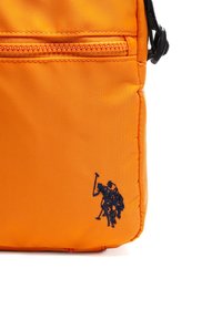 Orange nylon taske med en tekstureret overflade, prydet med et lille marineblåt broderet logo af en rytter og en frontlomme med lynlås.