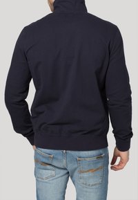 Mörkblå zip-up sweatshirt med hög krage, ribbade ärmar och midja. I kombination med ljusblå jeans i denim med sömnadsdetaljer.